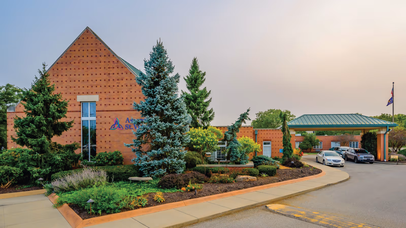 Brick senior living facility front with landscaped shrubs, trees, and a driveway entrance