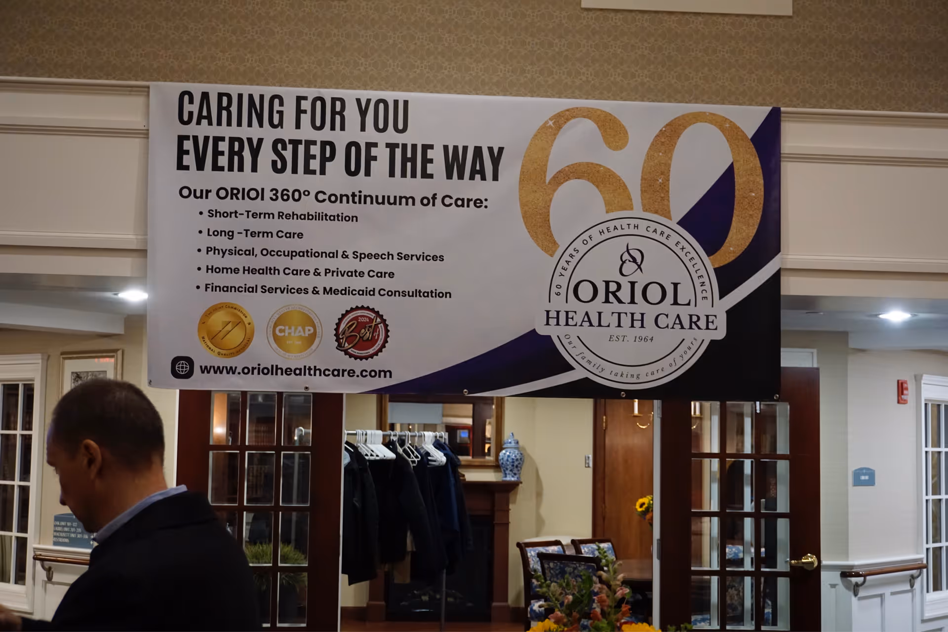 Large banner advertising Oriol Health Care hangs inside a facility lobby with a man nearby.