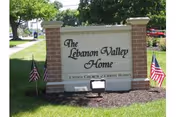 Brick sign reading The Lebanon Valley Home with American flags on both sides.