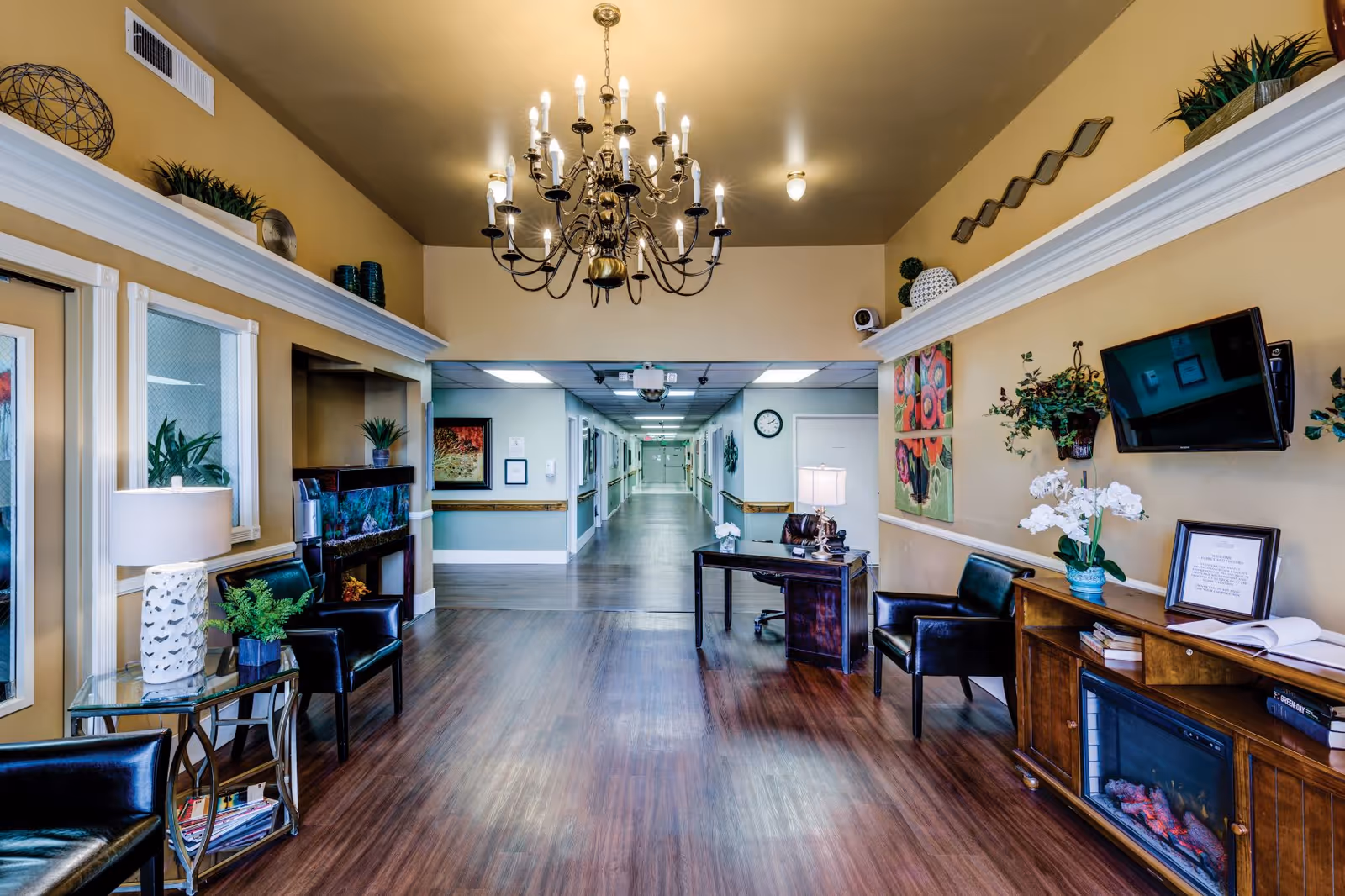 Luxurious senior living lobby with chandelier, long hallway, seating, plants, and a fireplace.