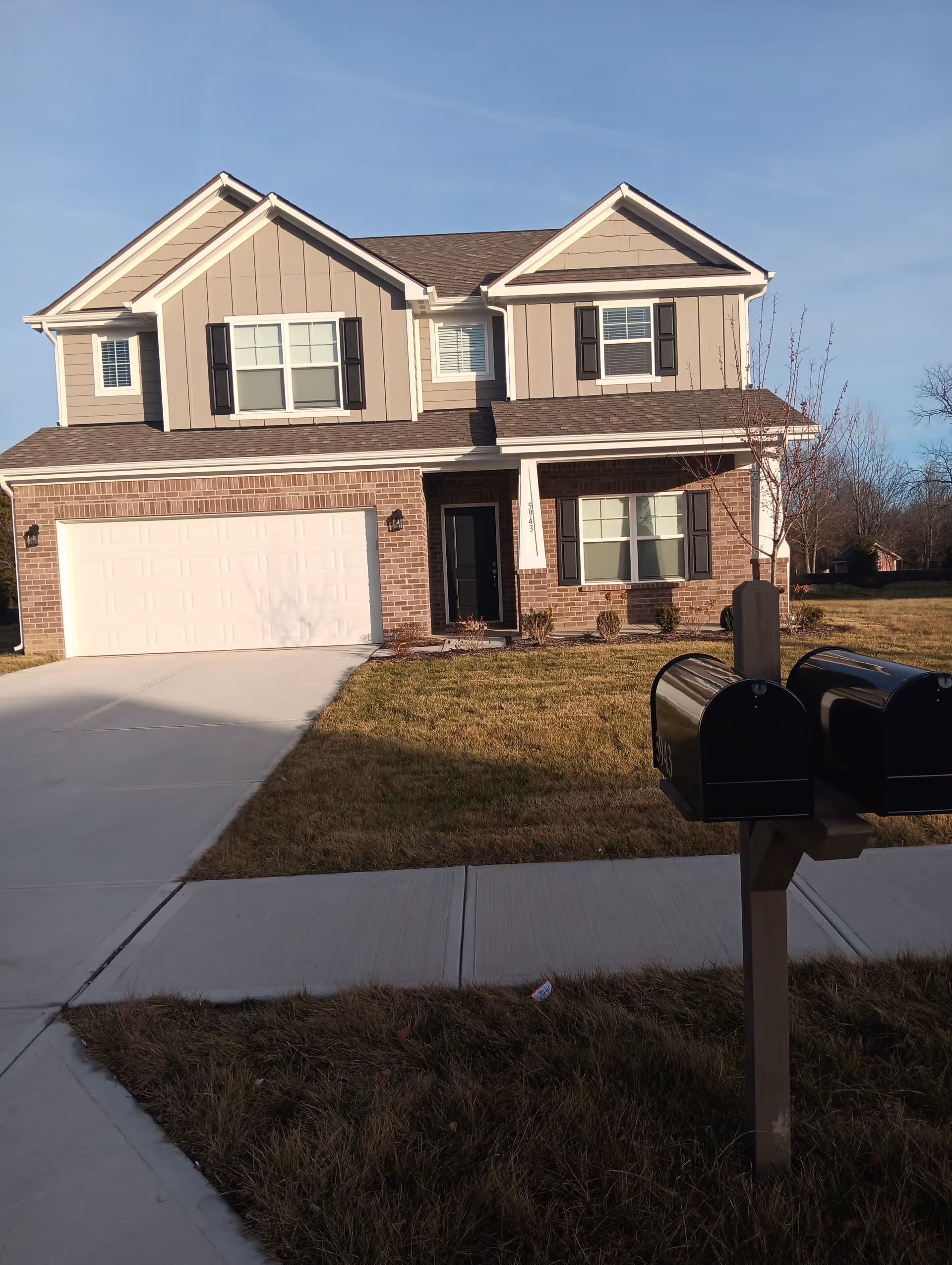 Two-story suburban home with brick lower level and beige siding, front yard, driveway, and mailbox.