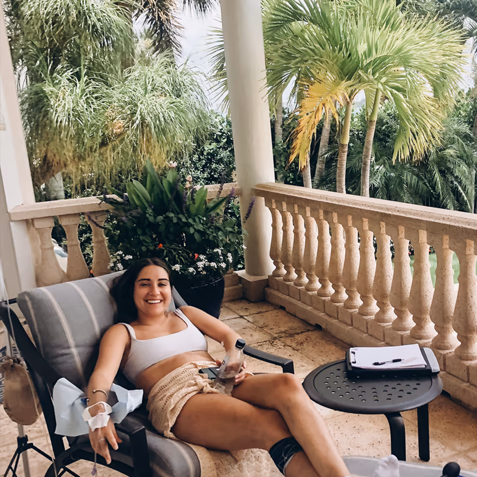Smiling woman relaxing on a patio lounge chair on a balcony with palm trees.