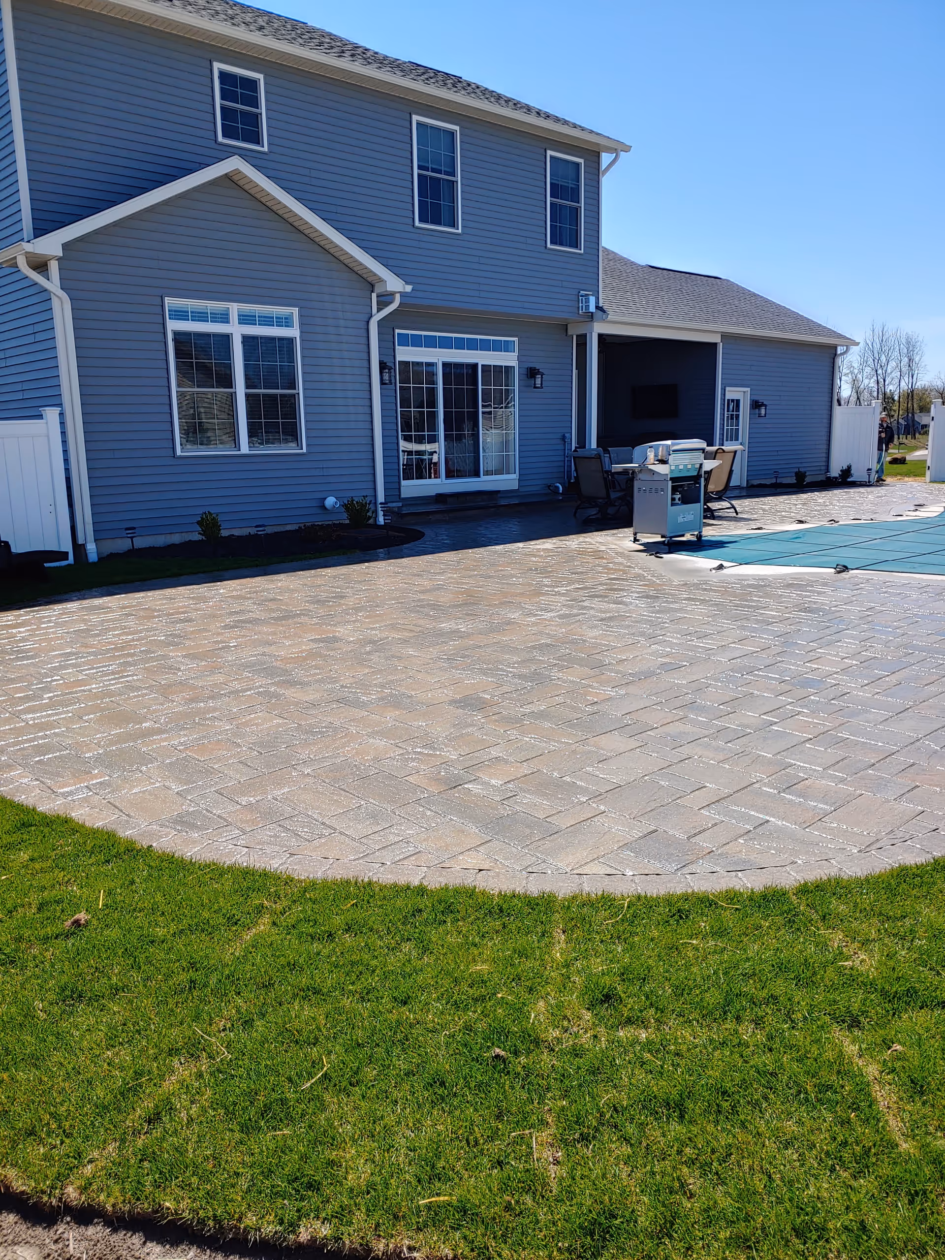 Two-story gray house with a large paved patio and outdoor grill seating area.