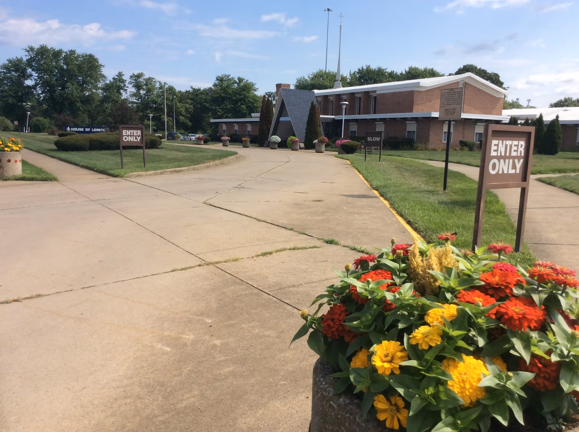 Exterior view of a brick senior living facility with enter-only signs and colorful flower planters