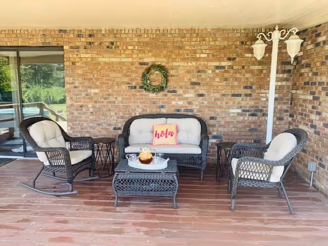 Outdoor patio with wicker seating, coffee table, and a wreath on the brick wall.