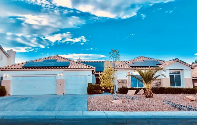 Single-story facility building with two-car garage, solar panels, and desert landscaping.