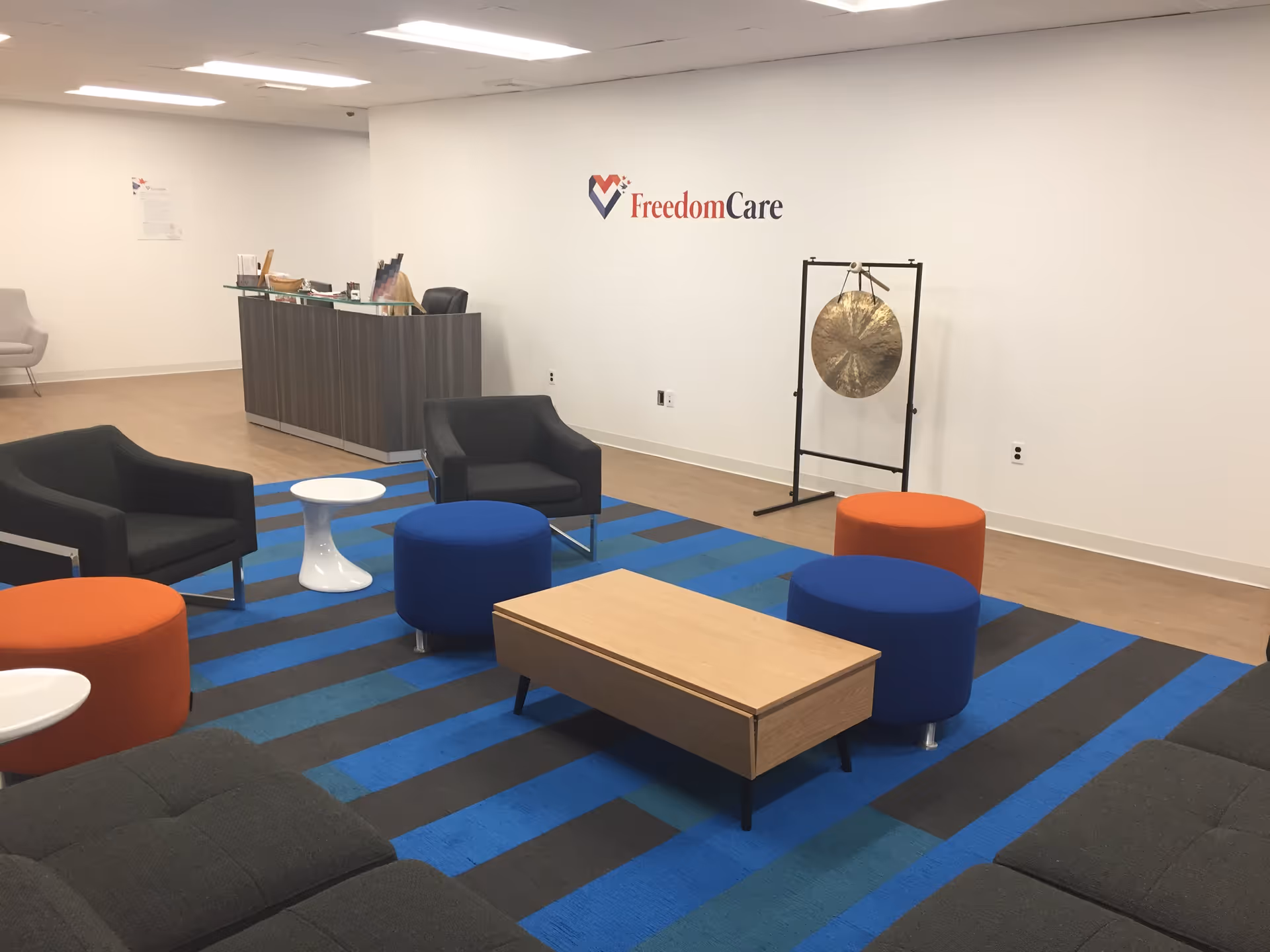 Reception area with seating, a desk, gong, and FreedomCare logo on wall.