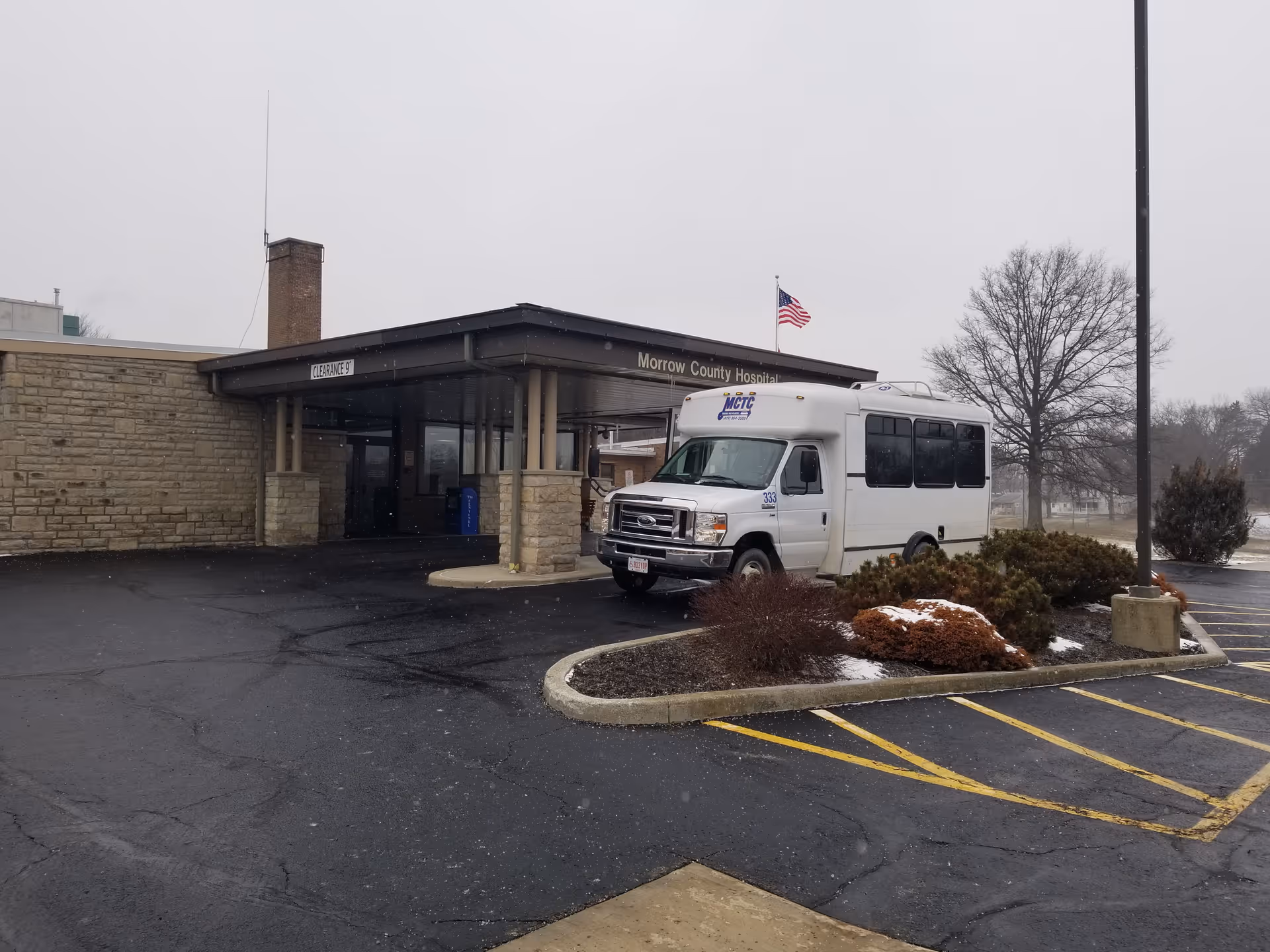 Exterior view of Morrow County Hospital entrance featuring a white shuttle parked by landscaping.