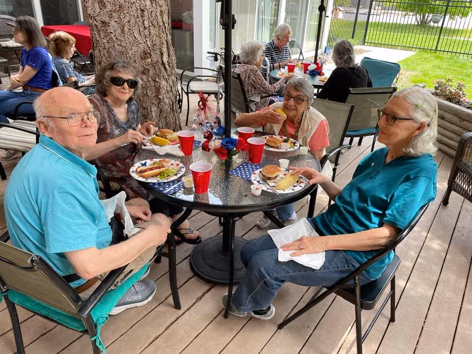Group of seniors at Cantril House enjoys a meal around a glass patio table outdoors.