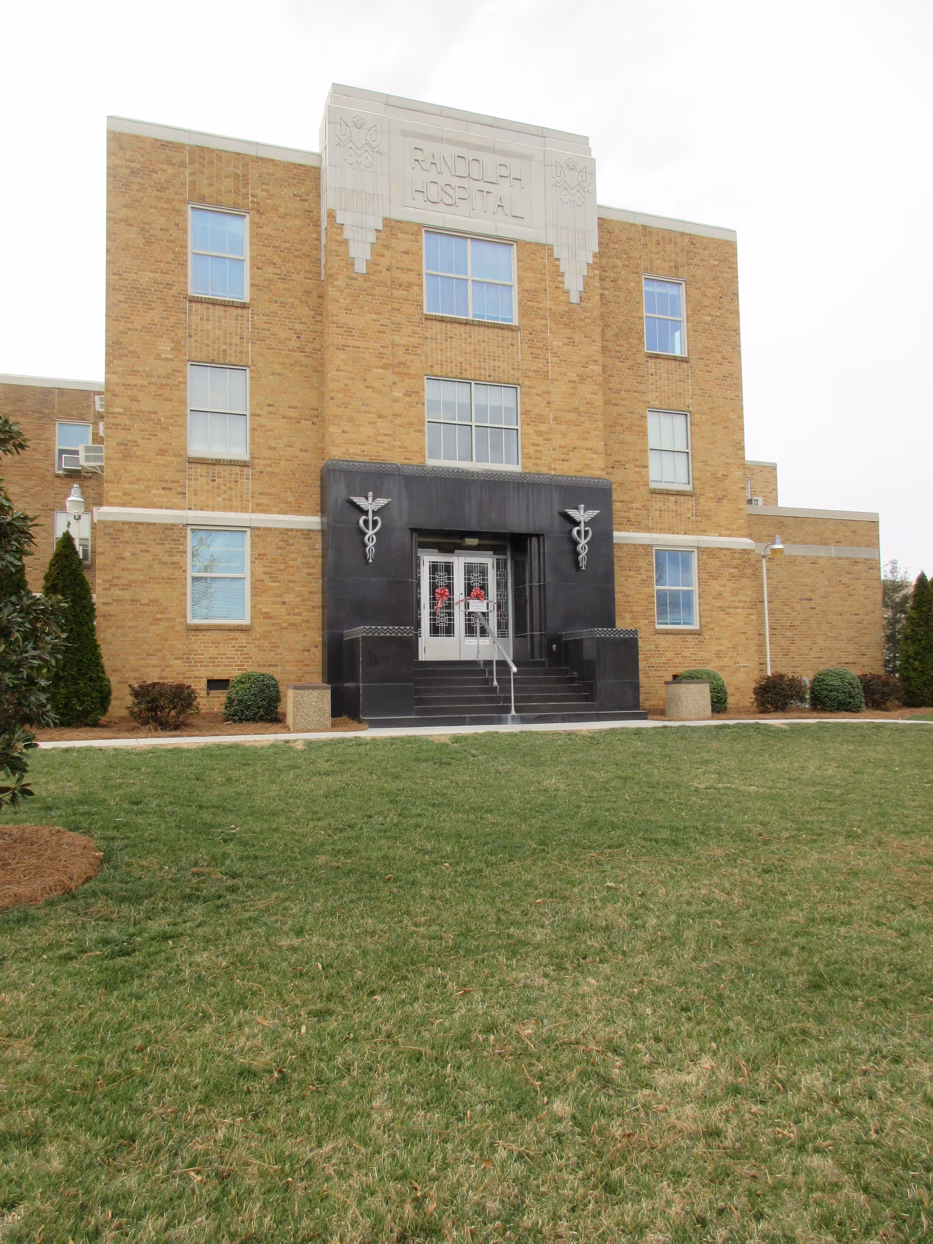 Brick hospital building with central entrance, stairs, and Randolph Hospital signage.