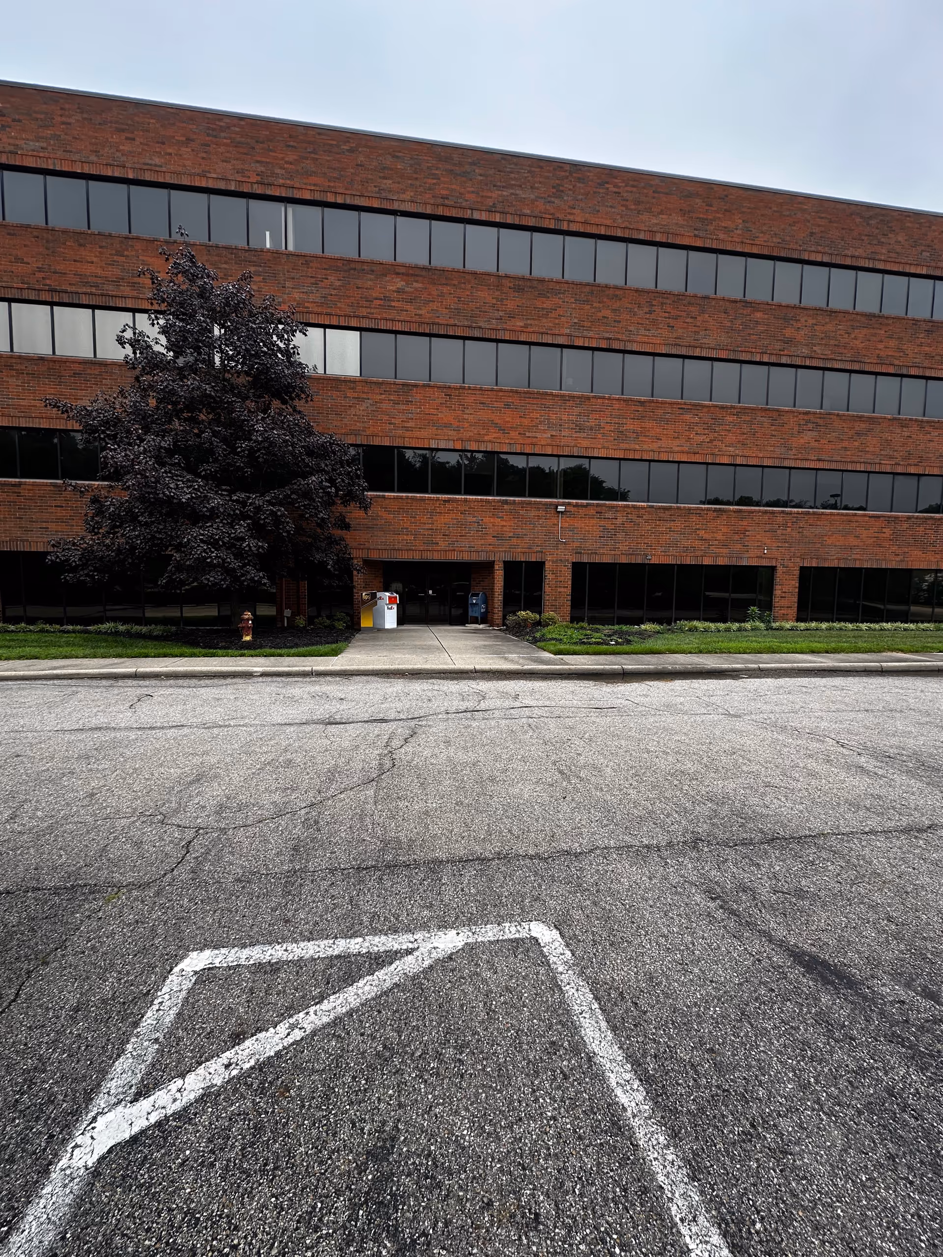 Brick office building exterior with many windows and a central entrance; parking lot in foreground.