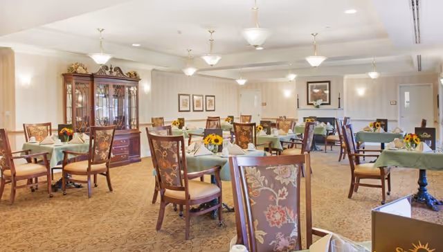 Spacious dining room with multiple tables, chairs, sunflowers, and soft lighting.