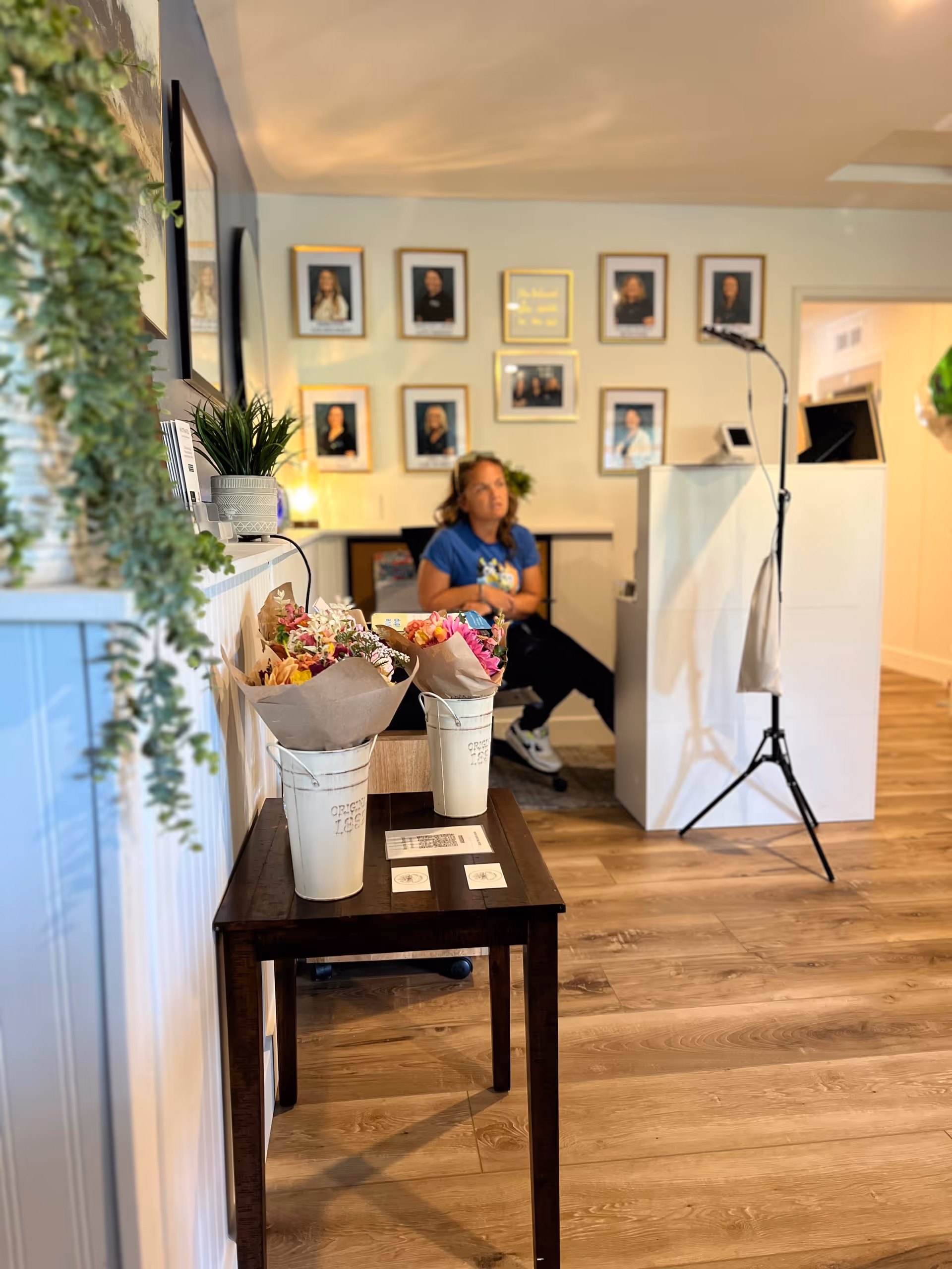 Reception area with a staff member at a desk, flowers on a table, and wall portraits.