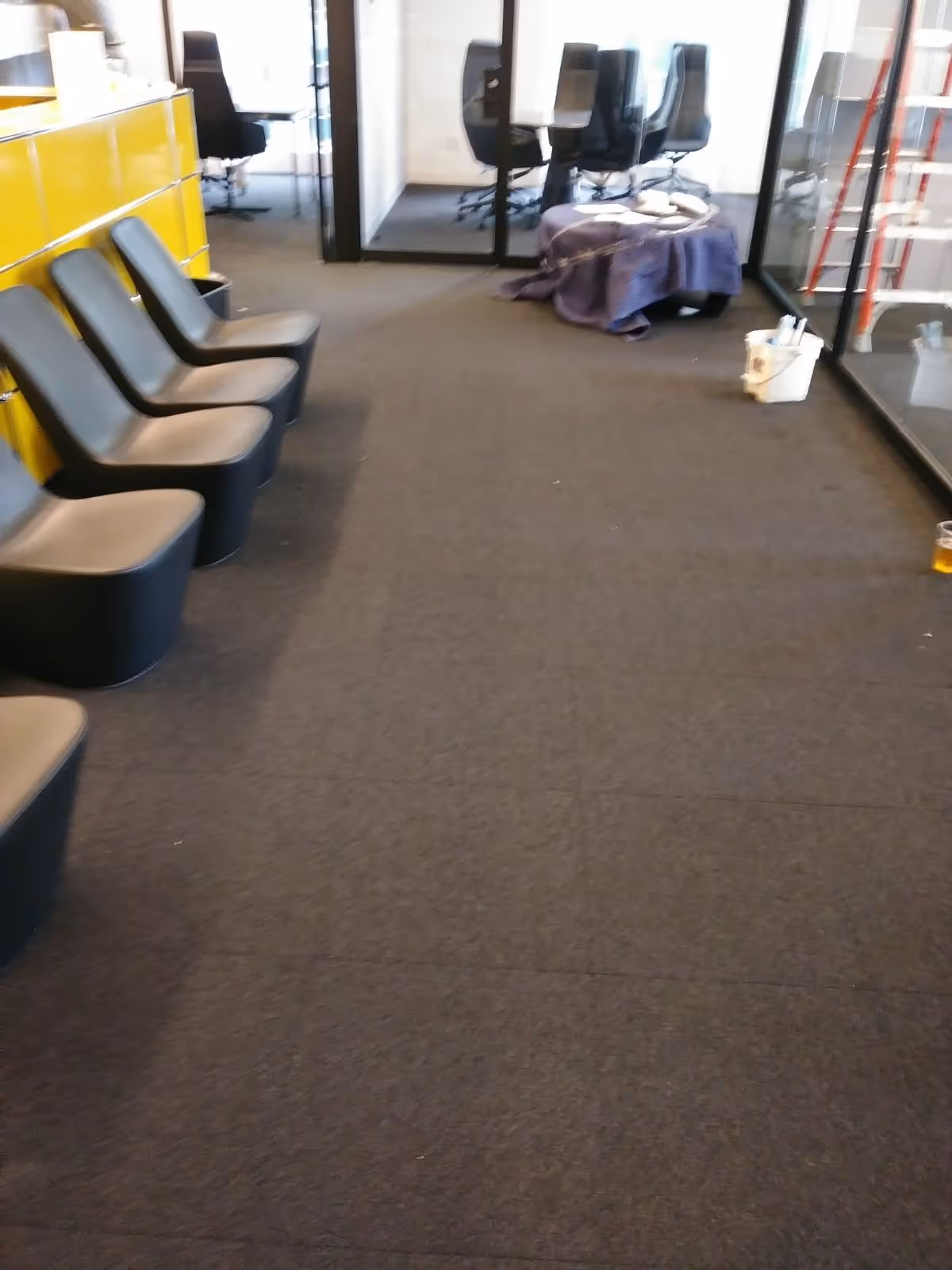 Indoor hallway with rows of black chairs, glass offices, and a purple-covered table.