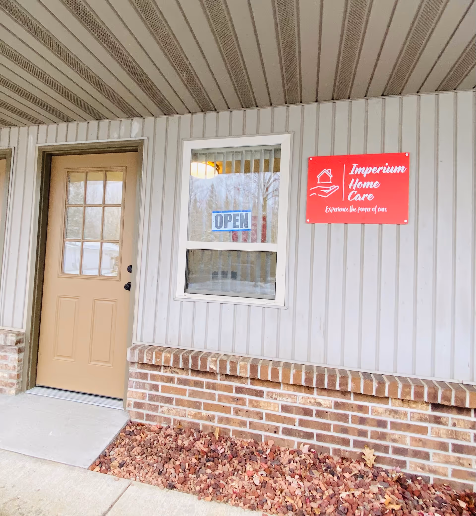 Exterior entrance of Imperium Home Care with OPEN sign, window, and brick siding.