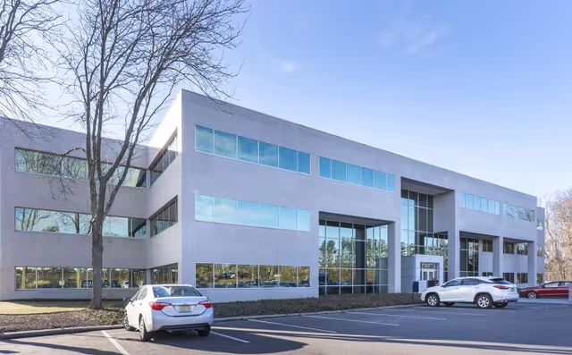 Modern two-story office building with glass facade and parked cars in a lot.