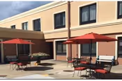 Outdoor dining courtyard with red umbrellas, tables, and chairs by a beige building.