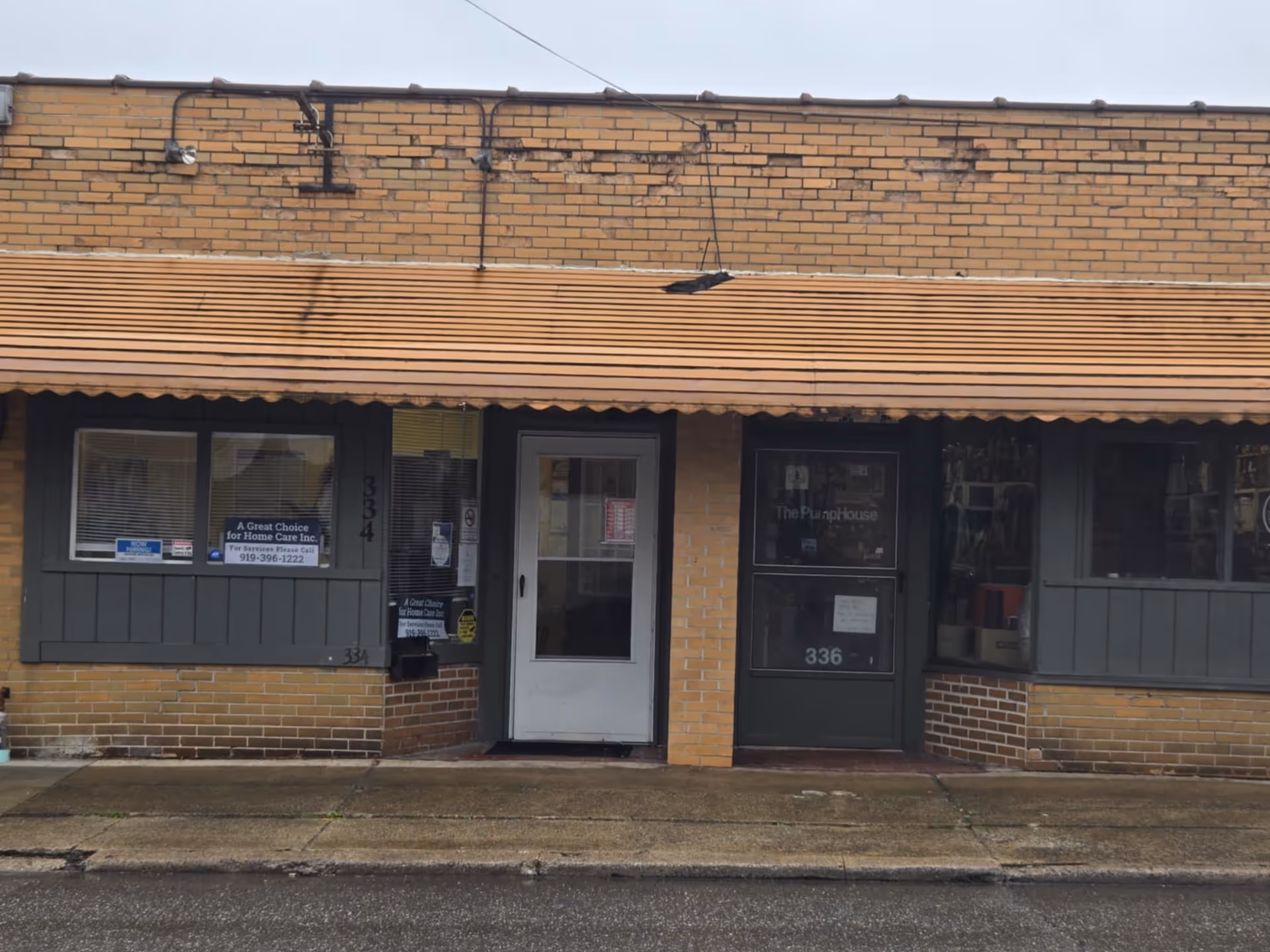 Brick storefront with two doors and windows facing the street in a small commercial building.