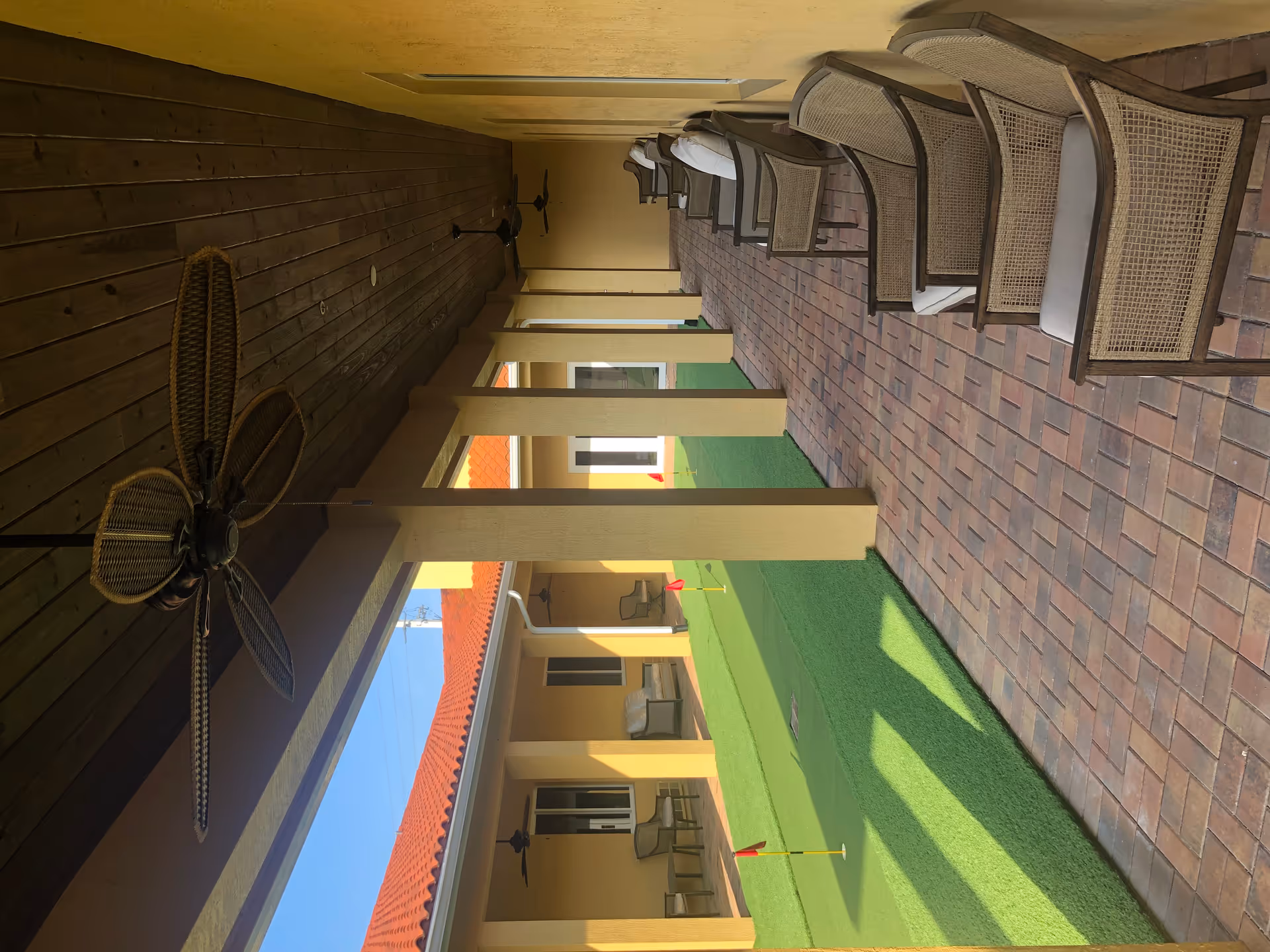 Covered outdoor patio with wicker chairs along a brick walkway and ceiling fans.