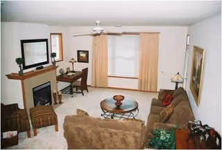 Cozy living room with brown sofas, a fireplace, coffee table, and window with beige curtains.