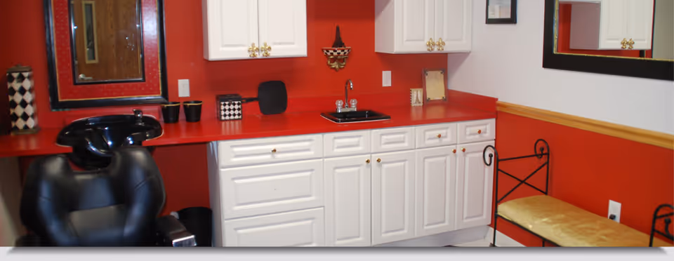 Interior salon area with a black shampoo chair and basin, white cabinets, red countertops and red-accented walls.