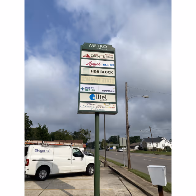 Tall outdoor signpost listing multiple businesses beside a street with a parked van