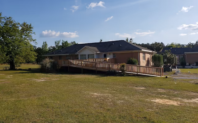 Single-story brick assisted living facility with a long wooden ramp and expansive lawn.