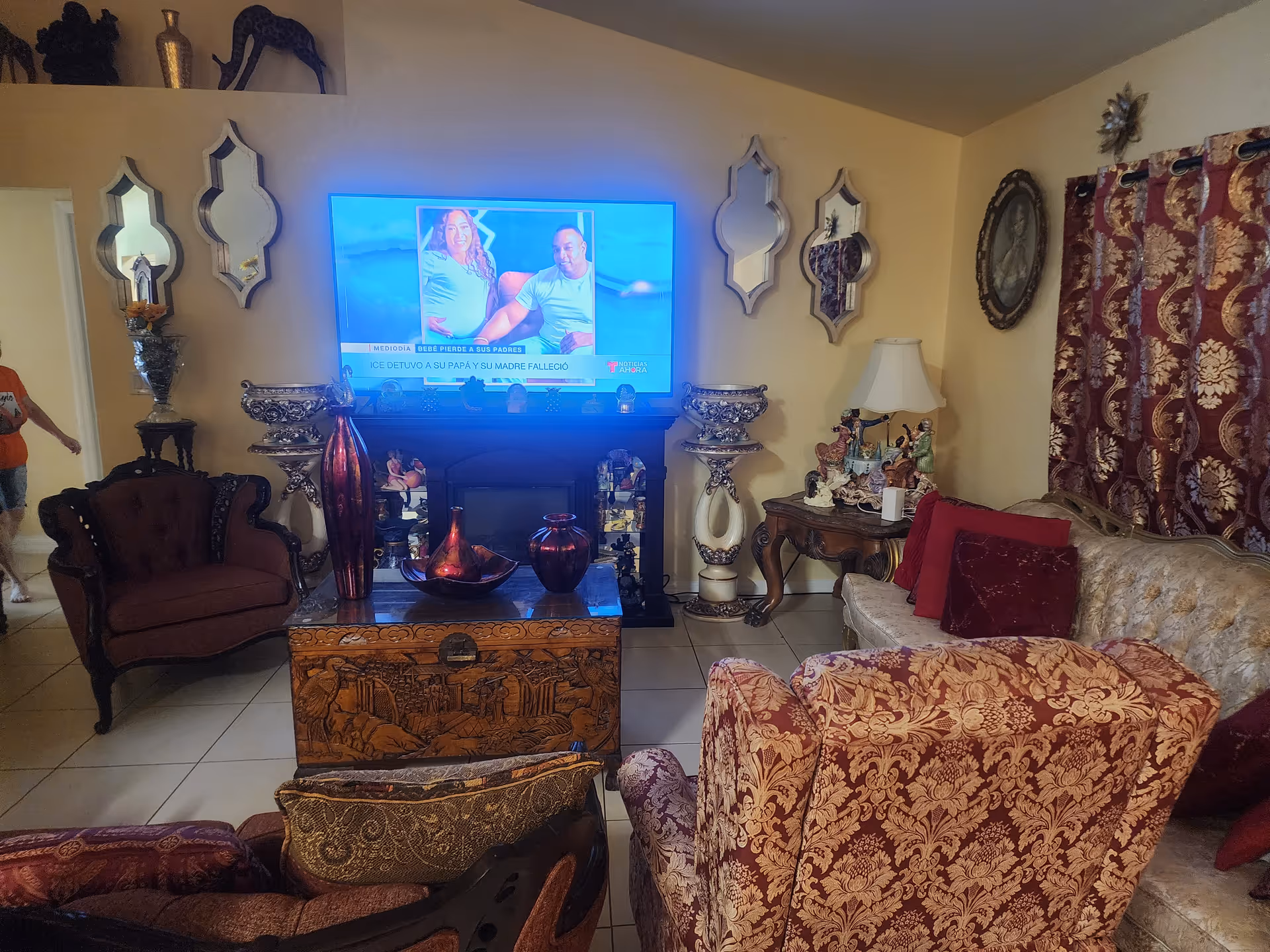 Ornate living room with patterned furniture, a TV on a stand, and decorative mirrors.