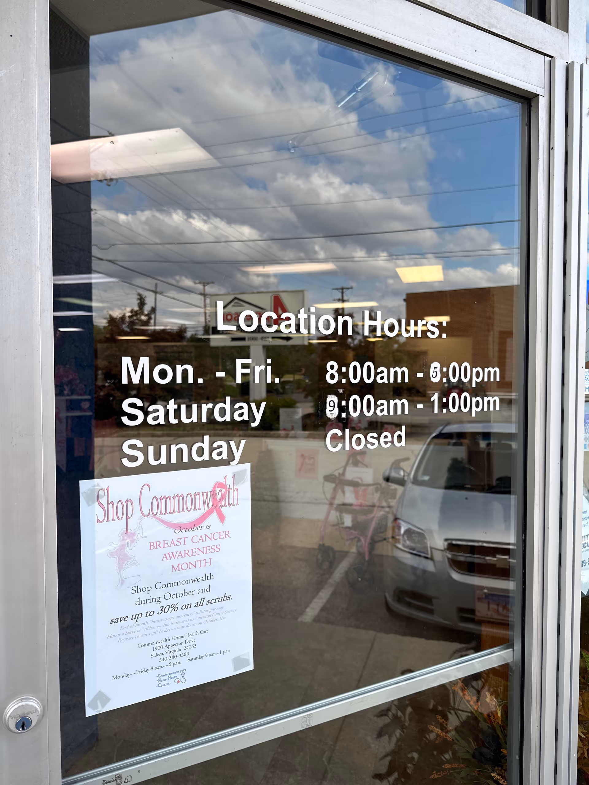 Glass door displays location hours and posters, reflecting sky and street.