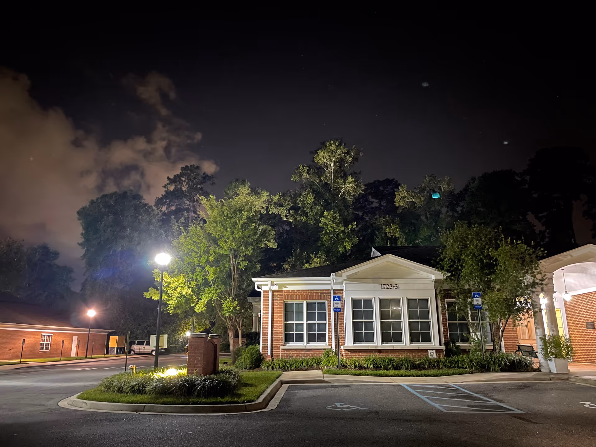 Night view of a brick hospice building with landscaping and parking in front.