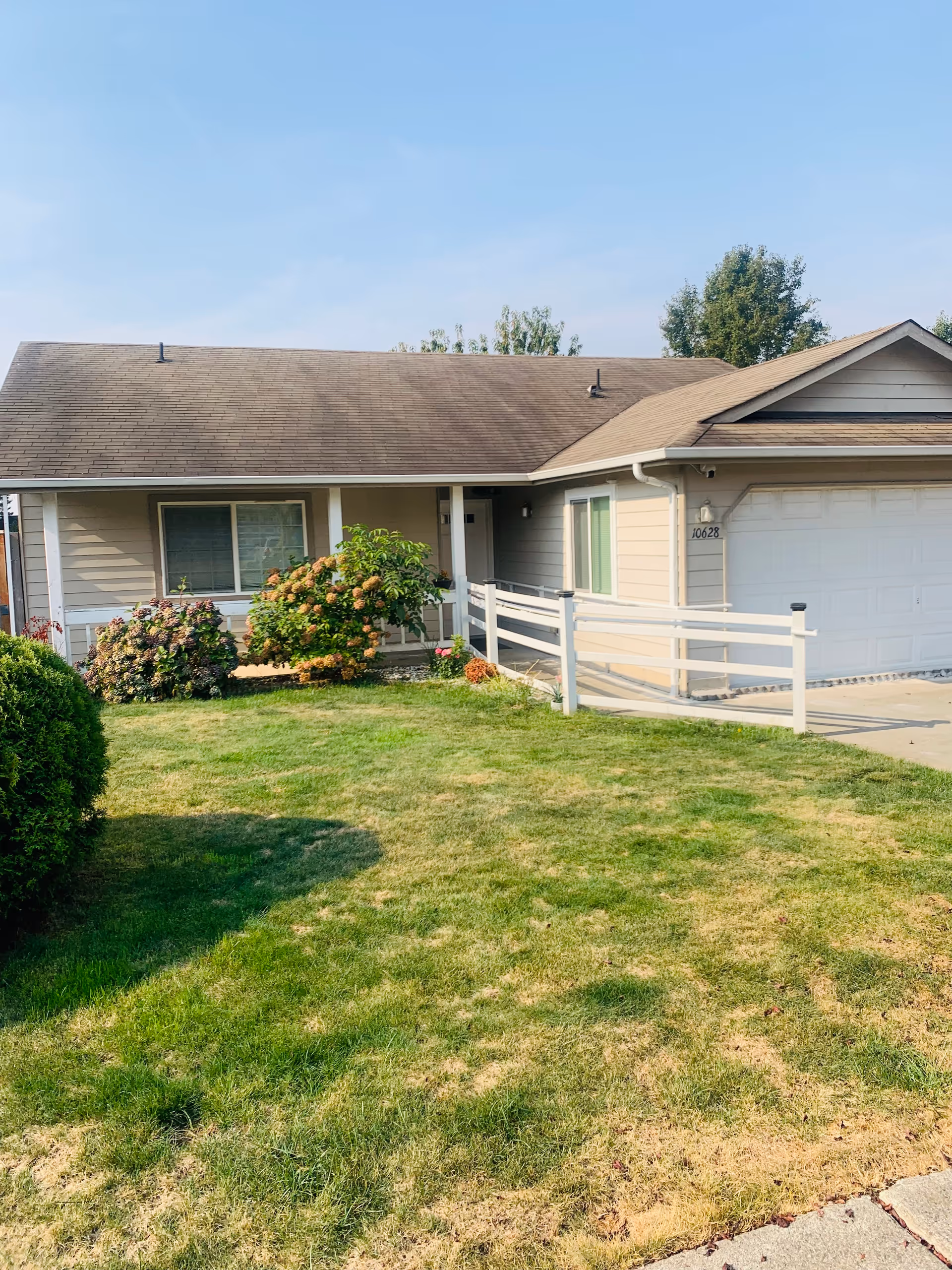 Front exterior of a single-story house with an attached garage, ramped entrance, shrubs and a grassy lawn.