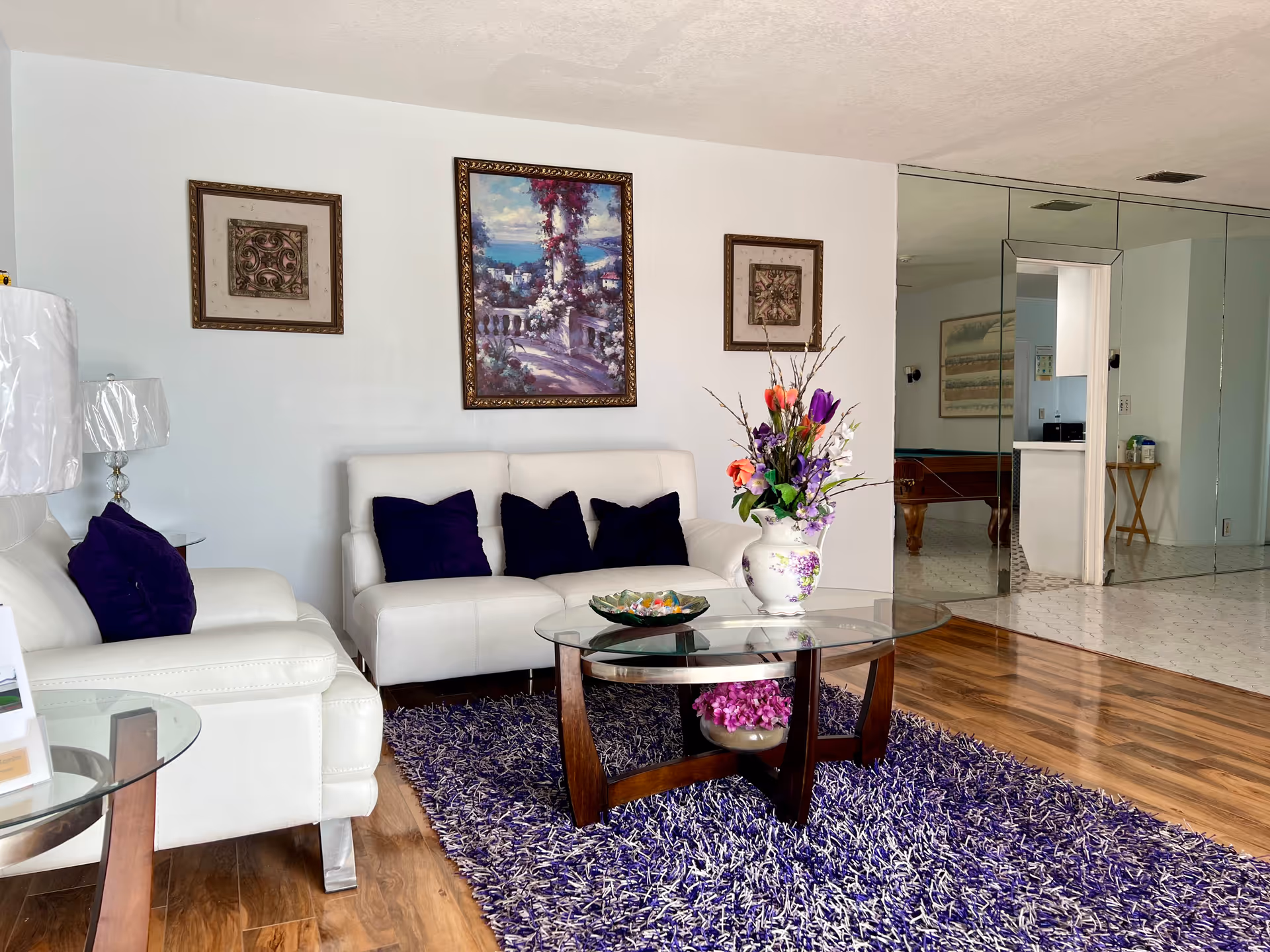 Cozy lobby seating area with white sofas, glass coffee table, and purple accents.