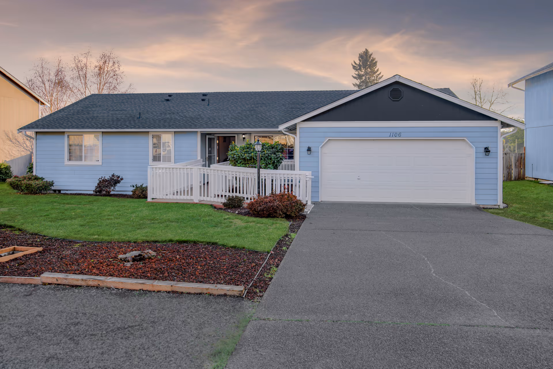 Blue single-story home with a front porch, white railings, and attached garage.