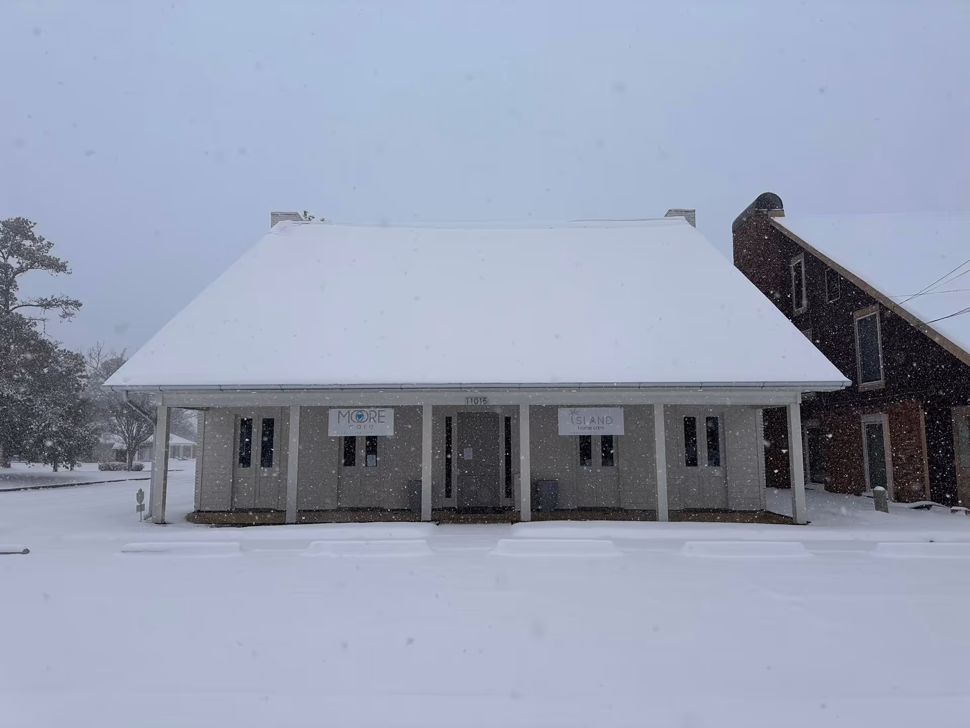 Snow covers a small front building with Moore Care caregiver services signs.