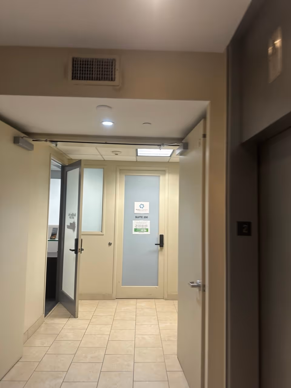 Narrow interior hallway in a facility with multiple doors and a tiled floor.