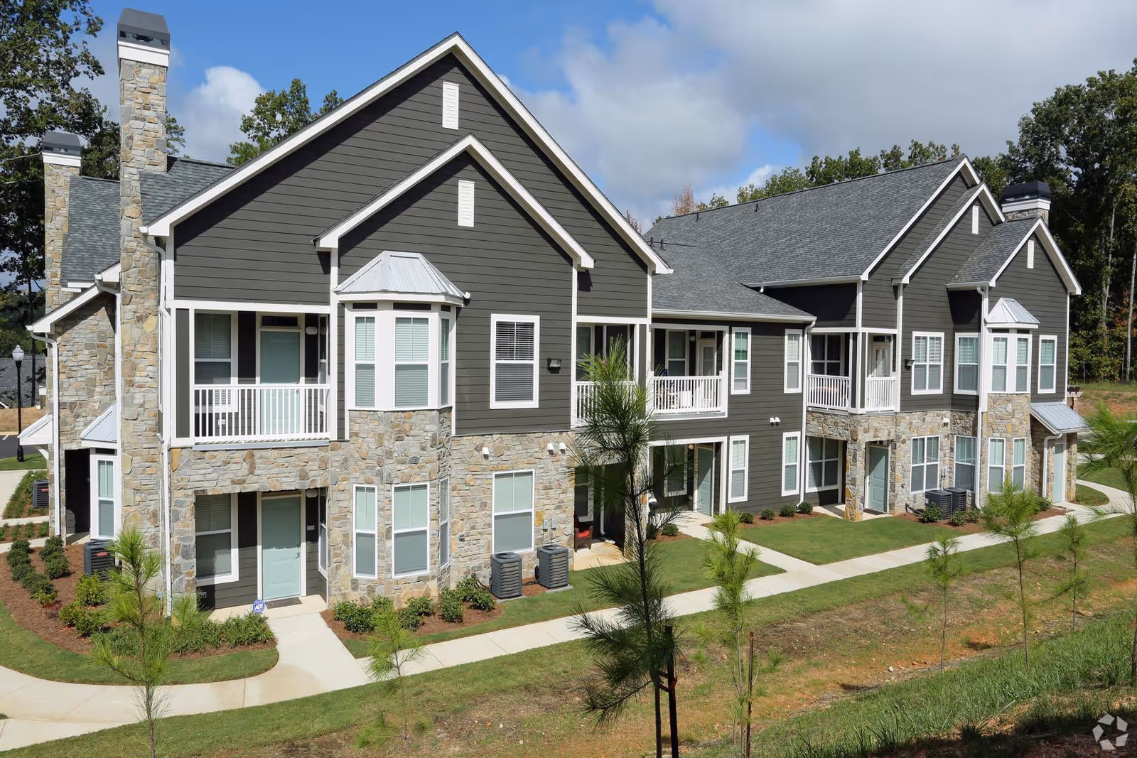 Two-story gray and stone apartment-style senior living building with balconies and landscaped walkways.