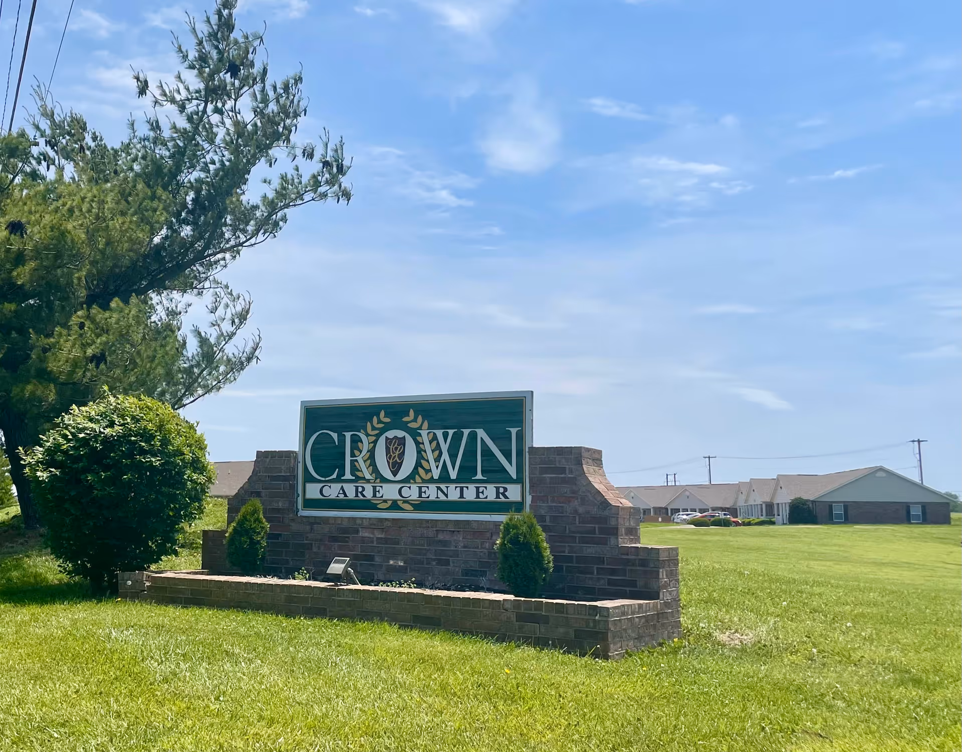 Crown Care Center sign on brick pedestal in sunny, grassy exterior.