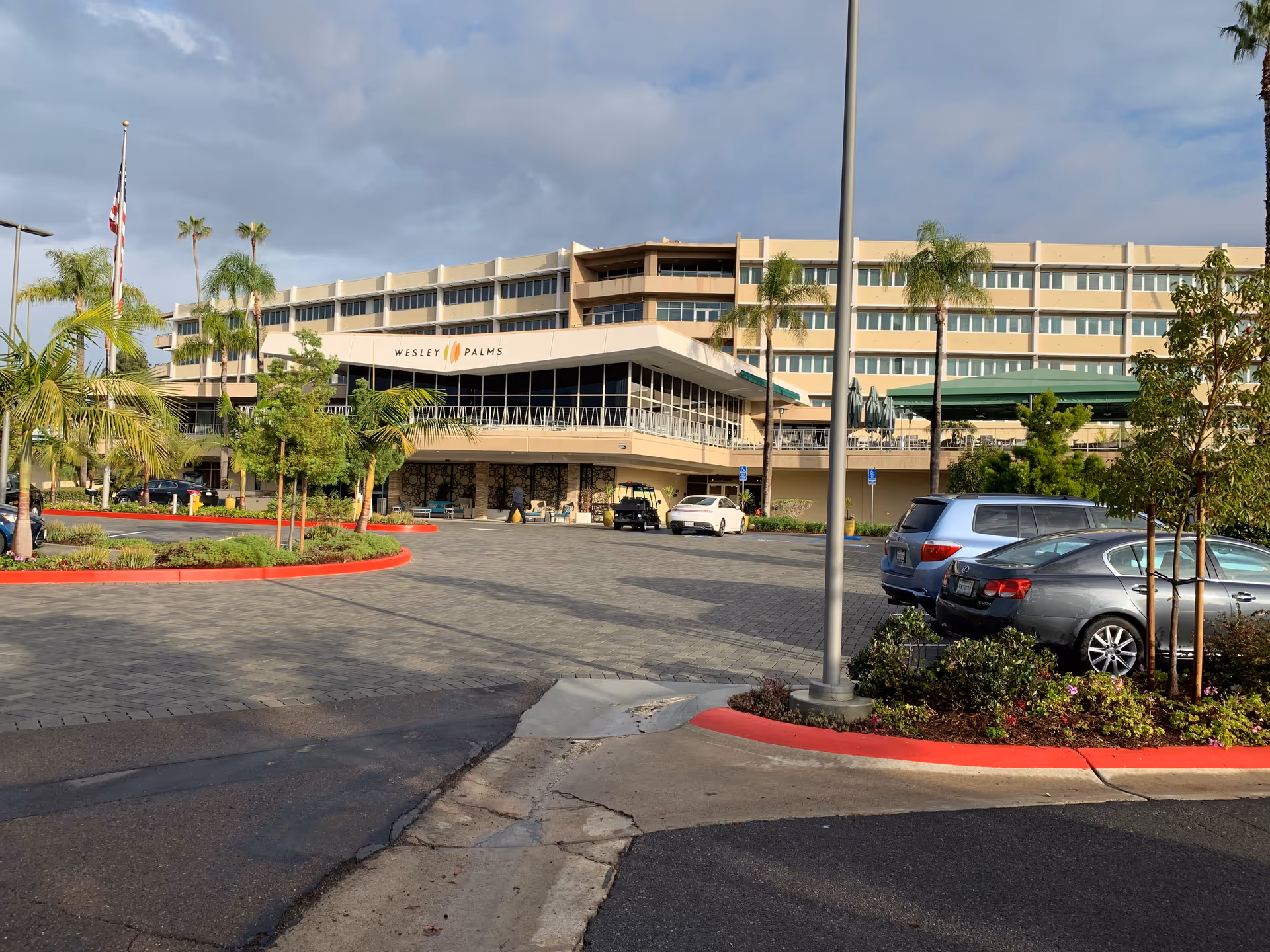Front entrance and parking area of the Wesley Palms Retirement Community building with palm trees and parked cars.