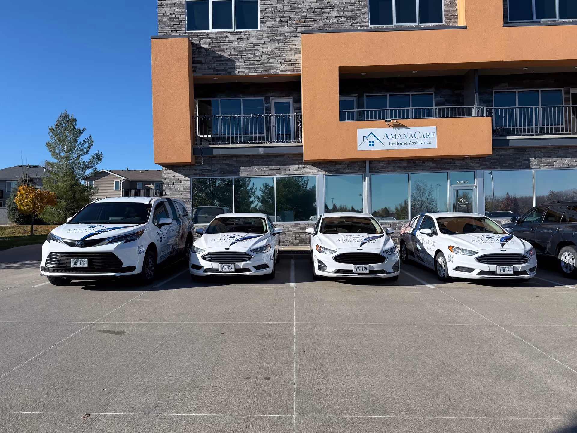 Exterior view of AmanaCare facility with cars parked in front.