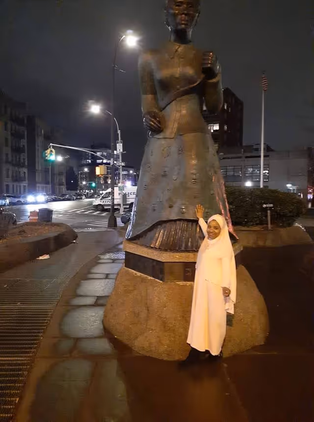 Nighttime street scene with a large statue and a woman in white posing beside it.
