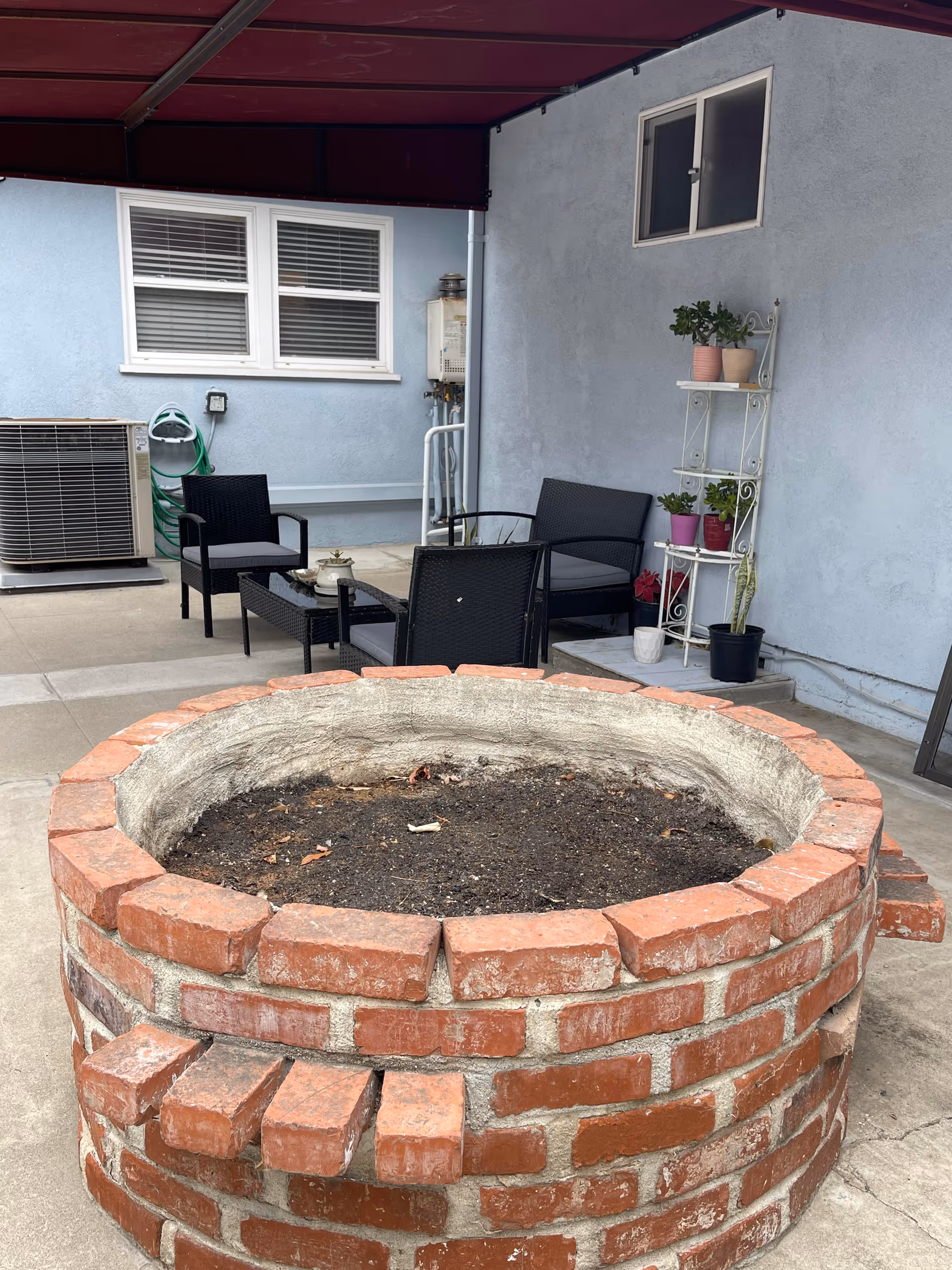 Outdoor patio with black wicker chairs, a table, and a large brick circular planter.