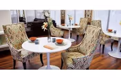 Round white tables with patterned chairs and floral centerpieces in a bright dining room.