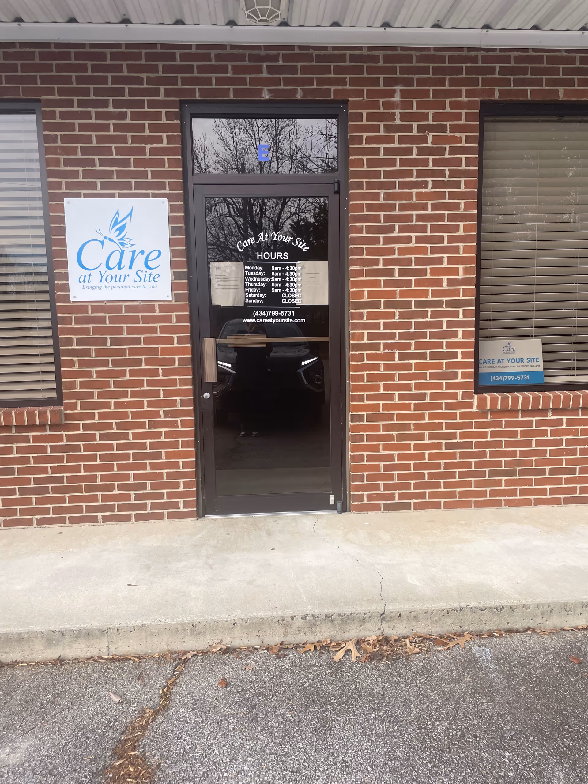 Brick facility entrance with glass door and Care at Your Site sign on the left.