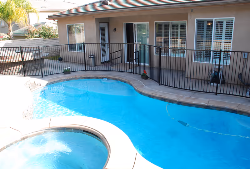 Exterior view of Eagle Glen Care Home pool area with a black fence and patio.