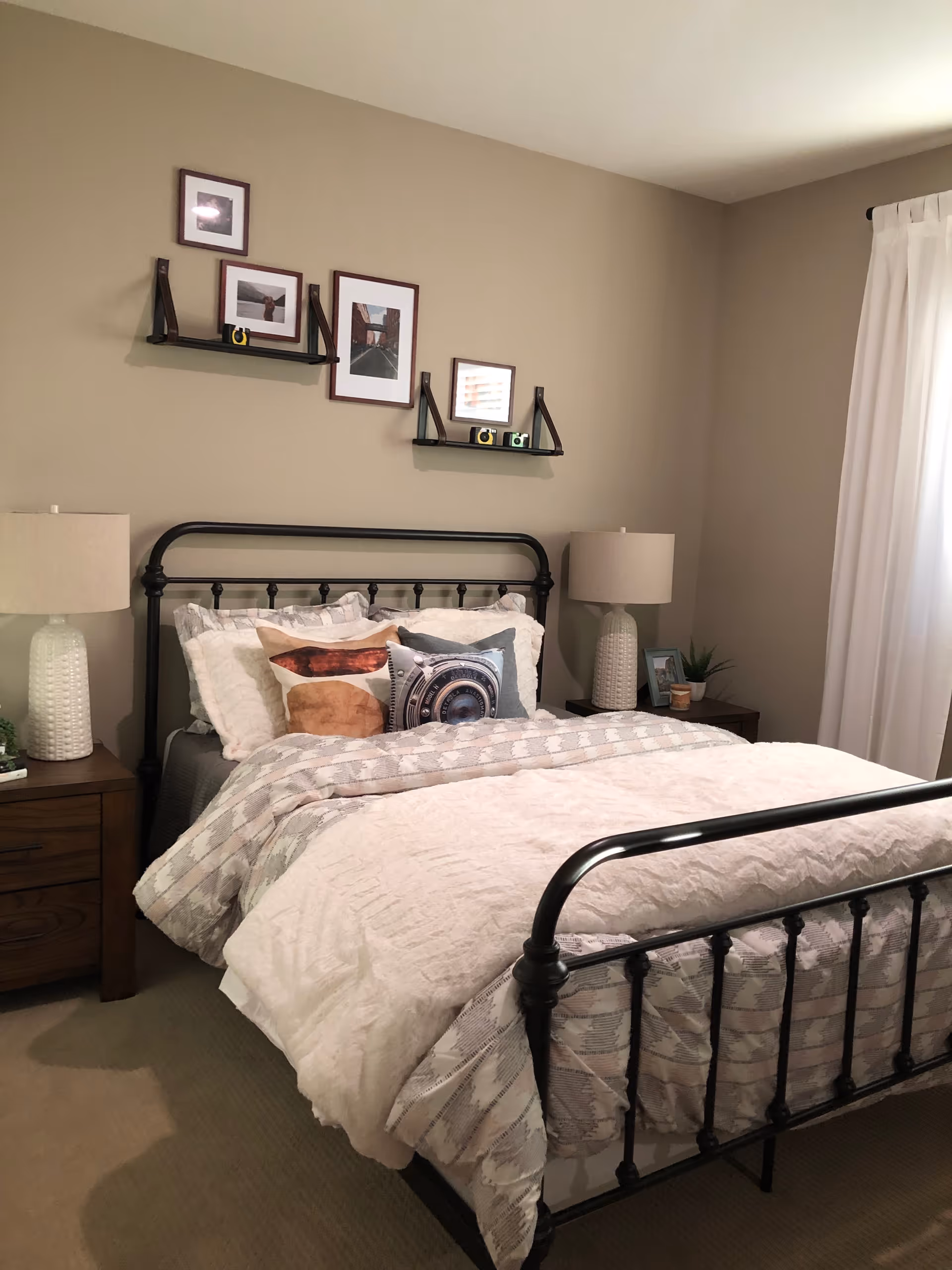 A neatly made bedroom with a metal-framed bed, nightstands, lamps, and wall art.