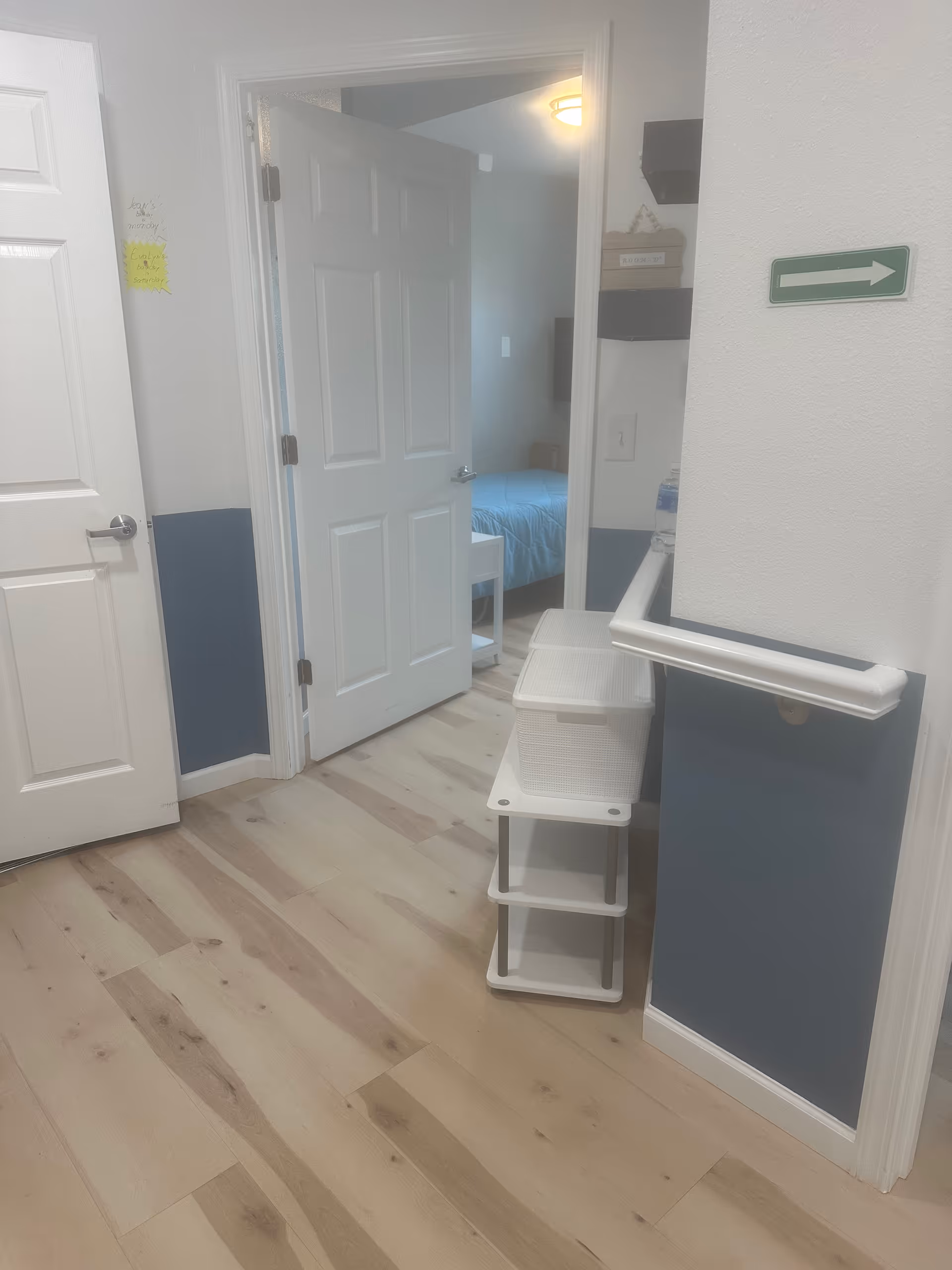 Hallway with light wood floor leads to a bedroom with a blue bedspread