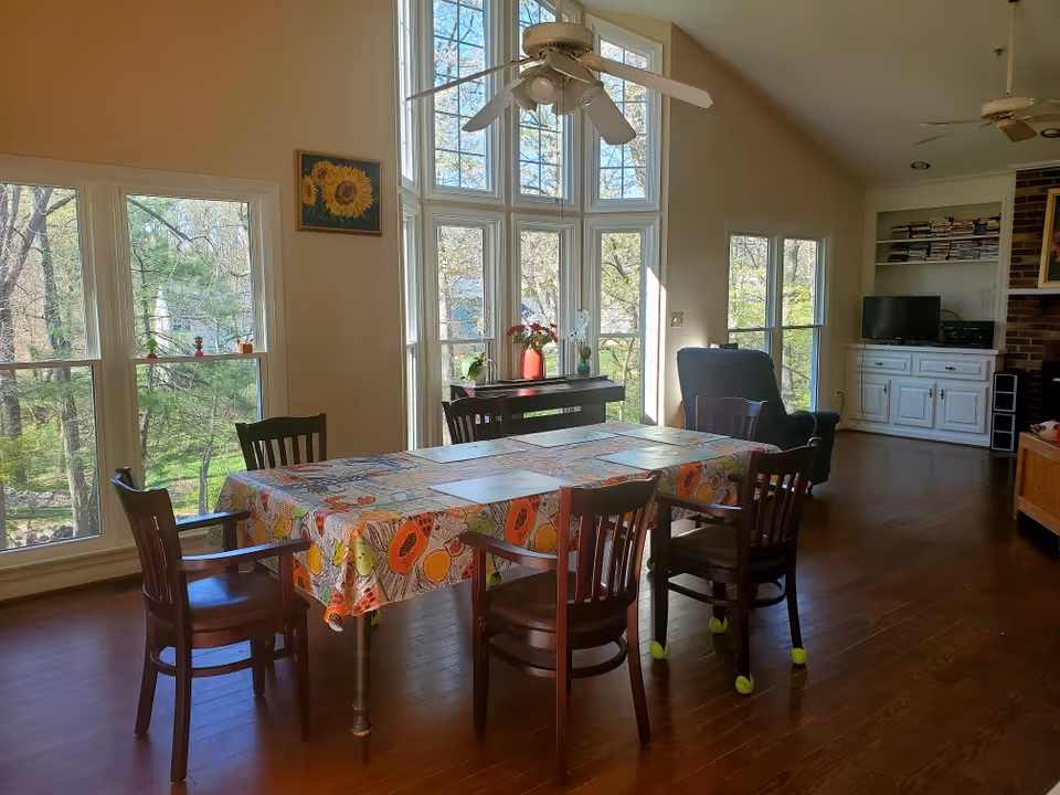 Bright dining area with a long table, chairs, and large windows in a cozy living space.