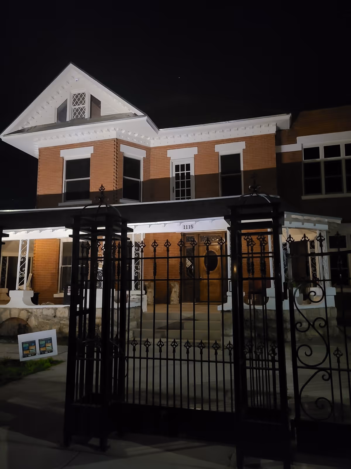 Night view of a brick senior living facility with a wrought-iron gate at the front.