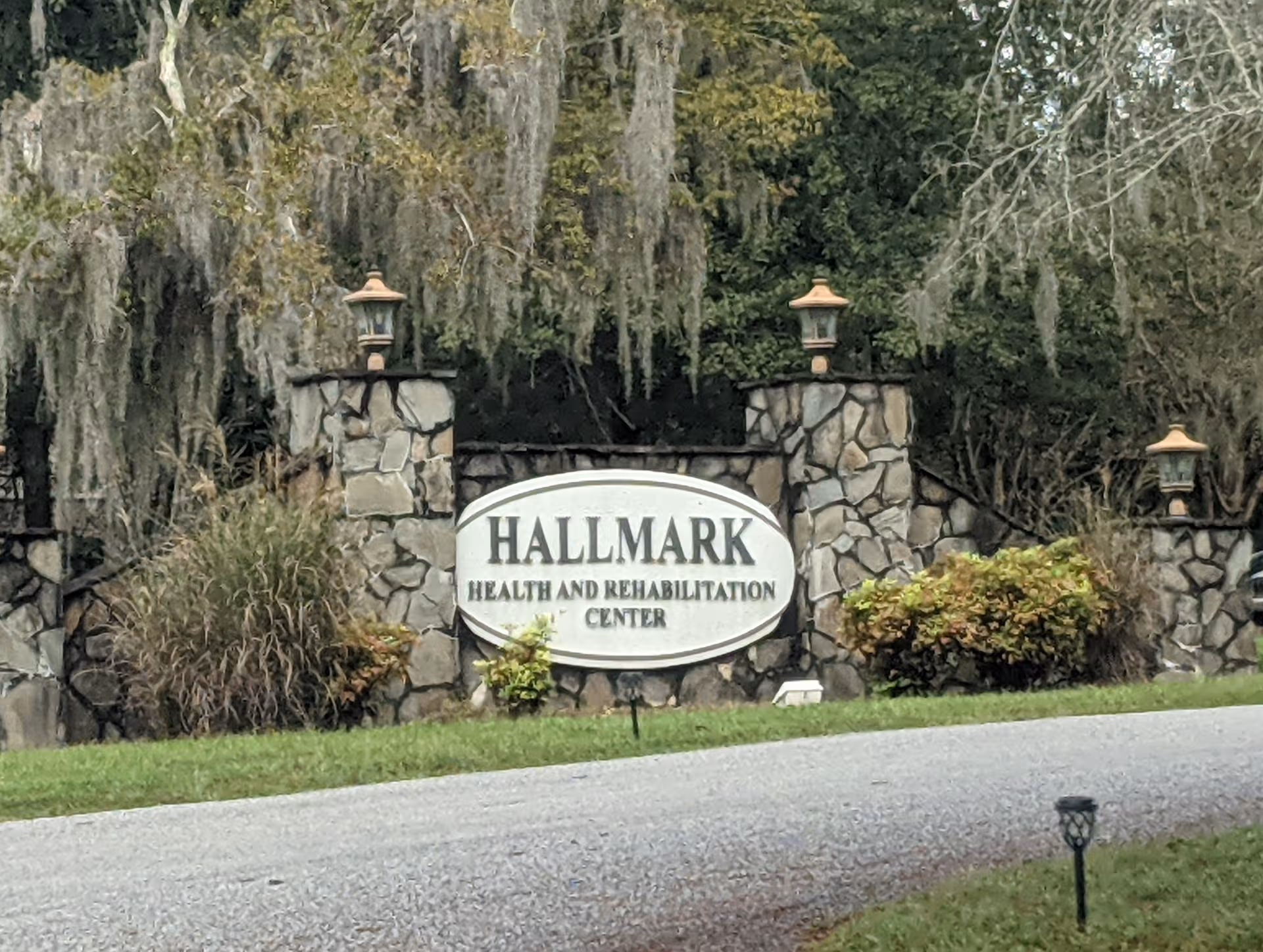 Stone entrance with Hallmark Health and Rehabilitation Center sign by a driveway.