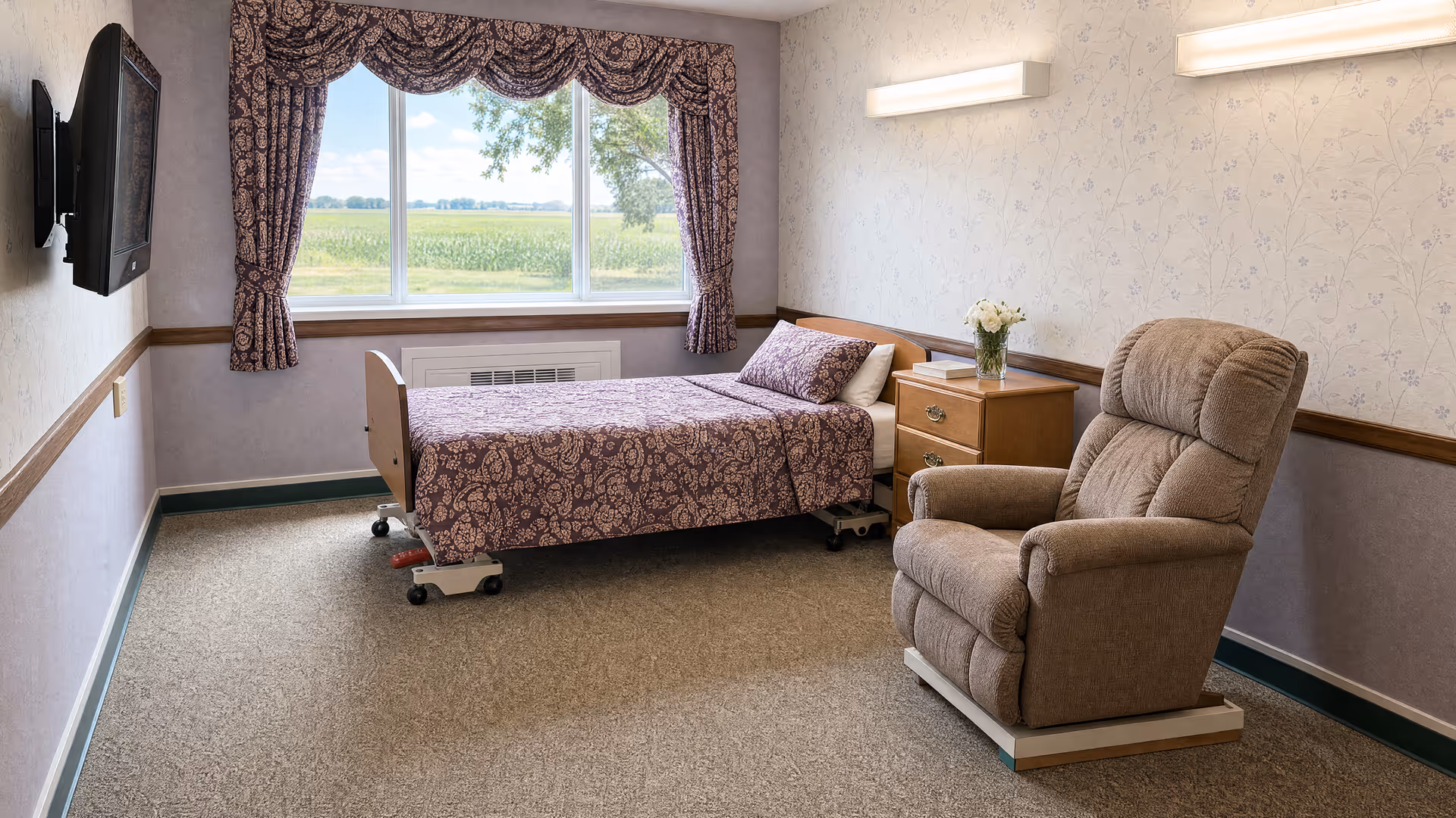 A cozy assisted living bedroom with a bed, recliner, nightstand, and window view.